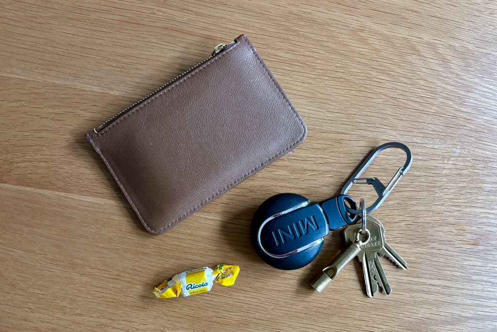 Clockwise from left: a brown leather wallet, a keychain for the Nite Ize G-Series double-chamber carbine size 3, and a Ricola throat lozenge.