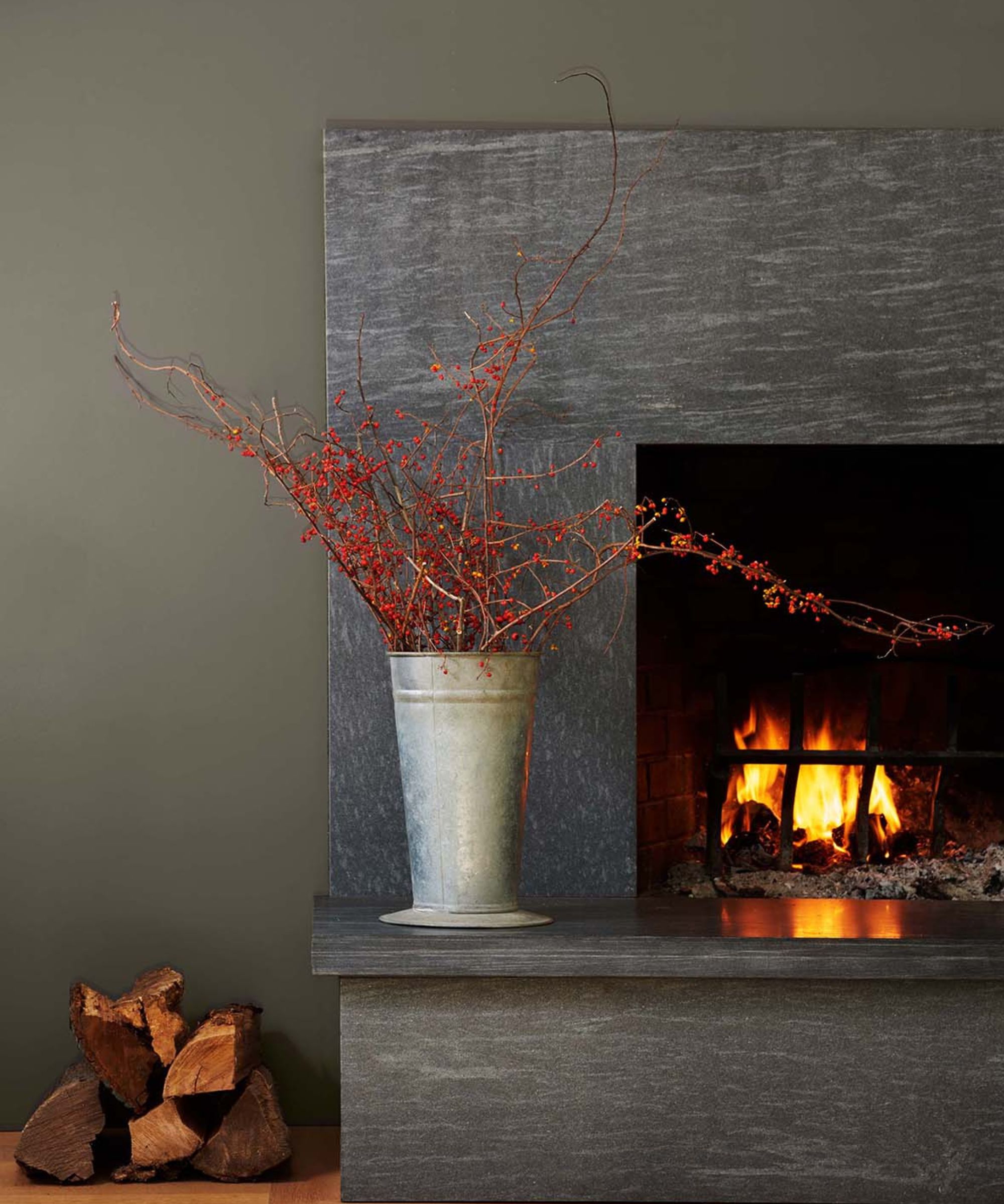 Gray -green wall with a fireplace, pot with red leaves, wooden stacks on the floor