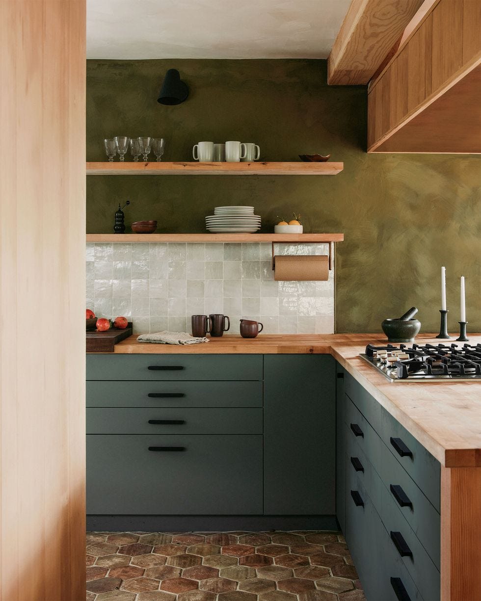 Kitchen from Studio Muka A kitchen with a stove tiled back splash in a white color dark green cupboards and a lighter green wall color