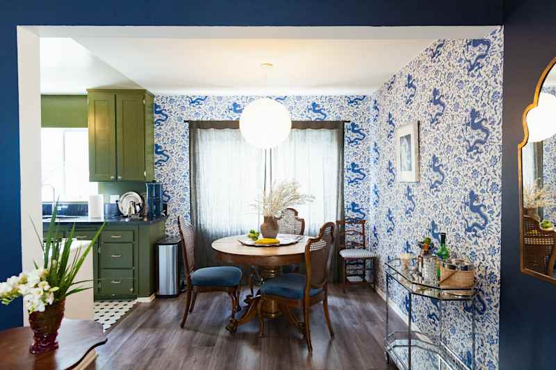 Cozy dining area with a round wooden table, four chairs, blue dragon wallpaper and a green kitchen in the background.