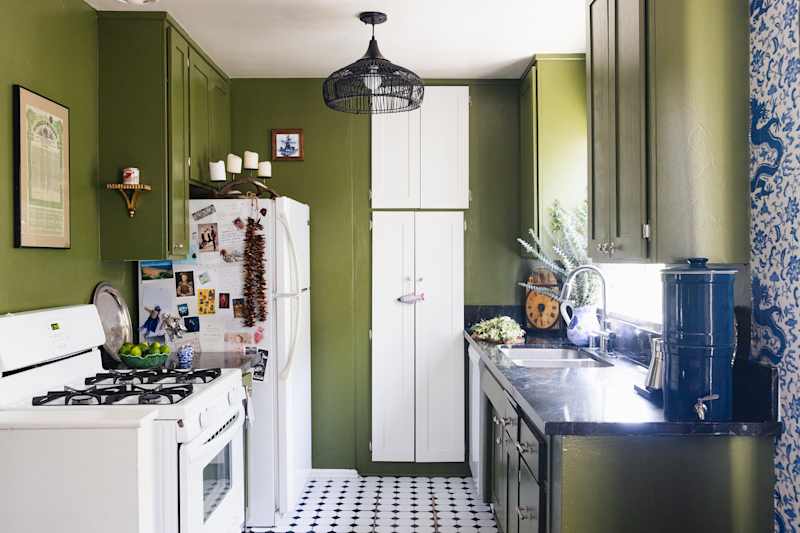 Cozy cuisine with green walls, white devices, black worktops and decorative objects such as plants and framed art.
