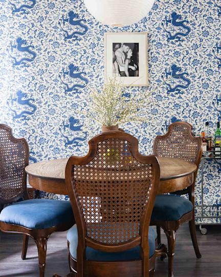 Dining area with a round wooden table, back-back chairs with blue pillows and a blue and white tapper.