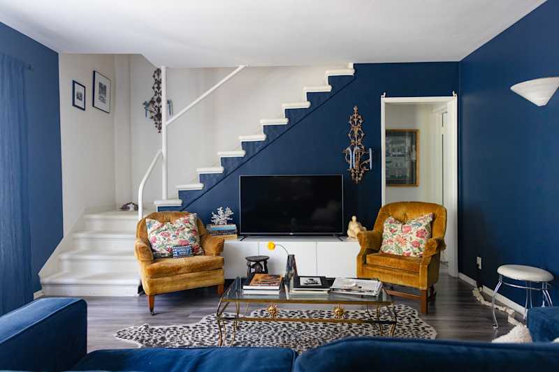 Cozy living room with marine walls, two old yellow armchairs, a glass of a glass table and a staircase.