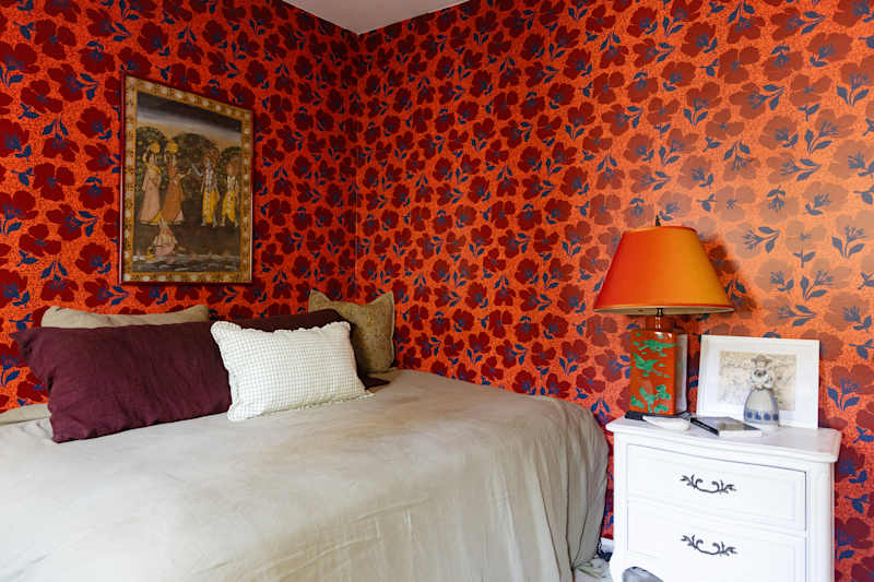 Cozy bedroom with lively flowers, a bed with decorative pillows and a bedside table with a lamp and framed art.