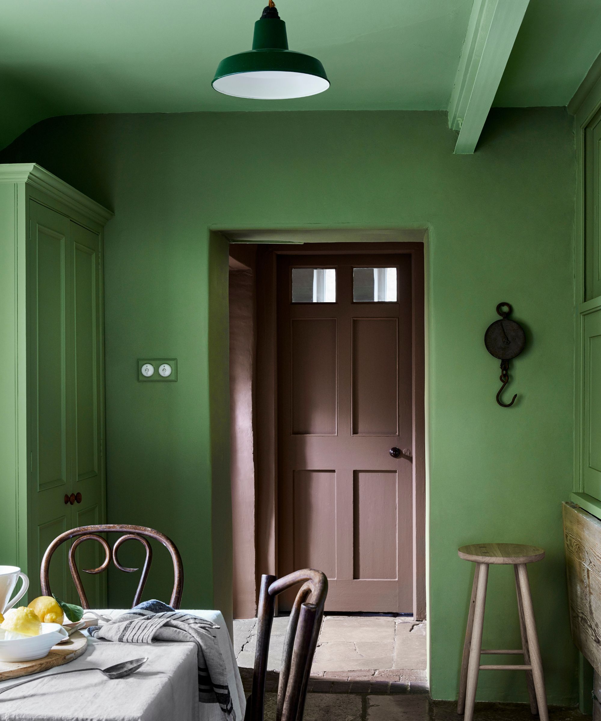 Kitchen with green, colored, soaked walls, stone floor, brown door and farm furniture