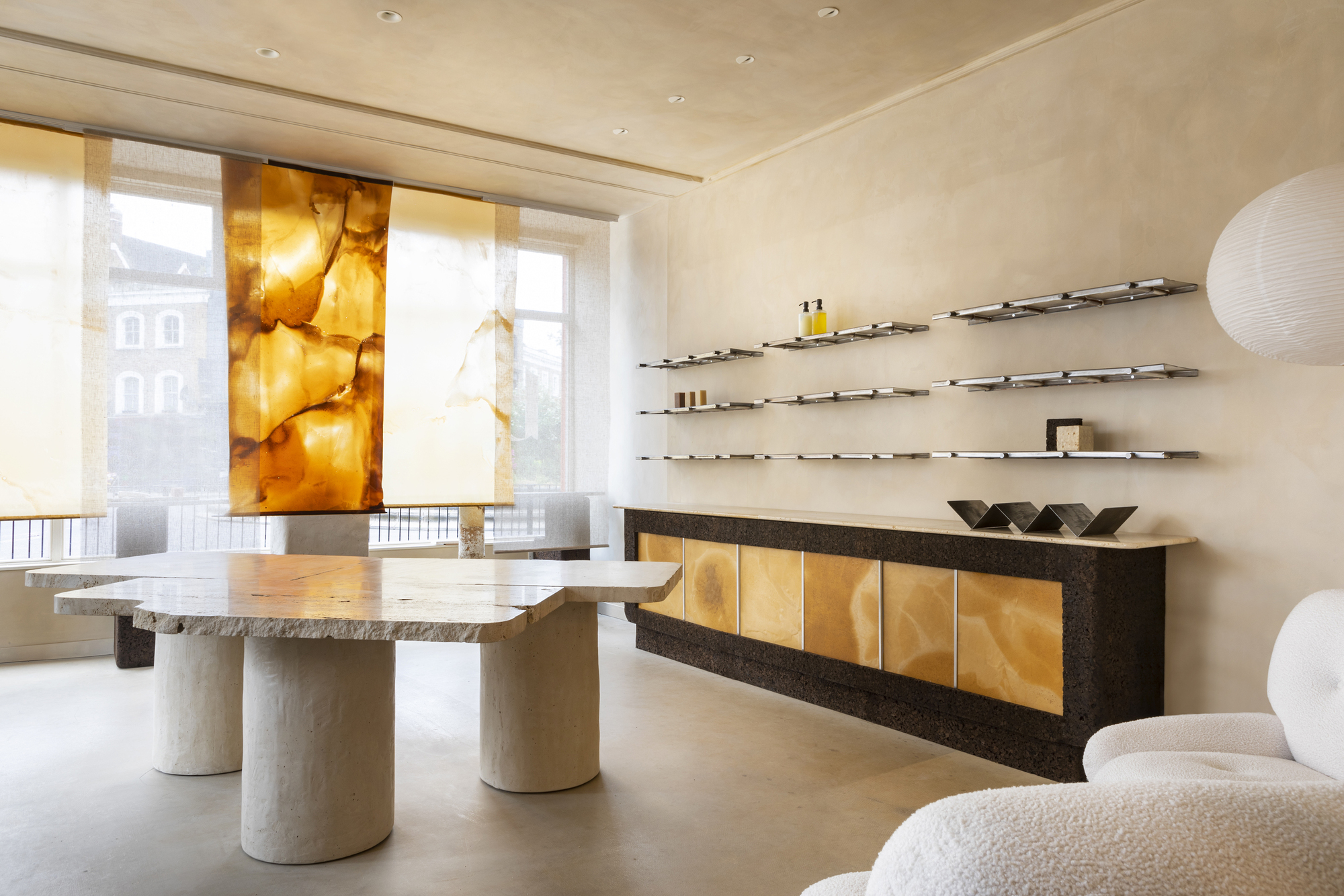 The inside of a beauty business with round -washed walls, a traverted table, floating shelves over a long console table and curtains that hang in the Shopfront window