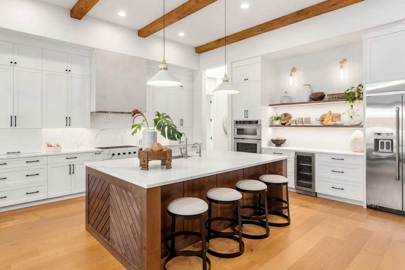 Beautiful white kitchen in the new luxury house with a large island. Has large island, stainless steel devices, wood accents and slim modern reach.