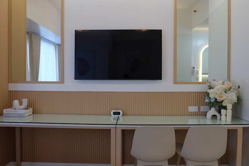 Modern work area with a glass desk, two chairs, a television and decorative flowers mounted on the wall.