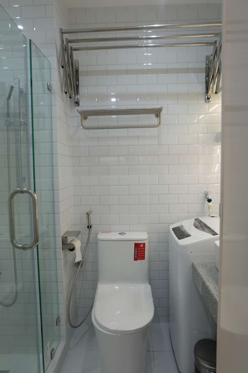 The compact bathroom with a glass shower, a modern toilet and a washing machine next to a granite worktop.