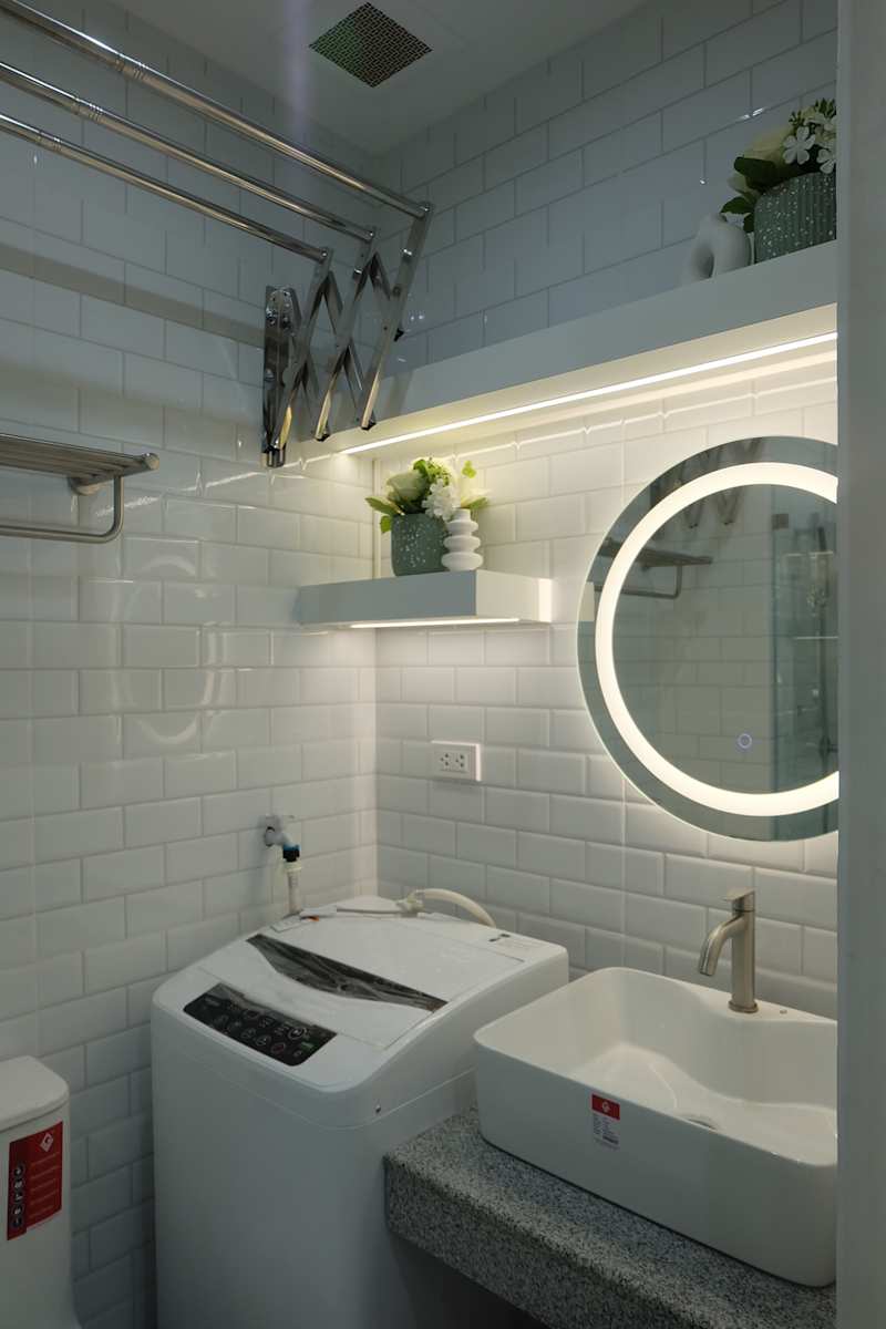 Compact bathroom with a washing machine, a modern sink, the round mirror with backlight and decorative plants.