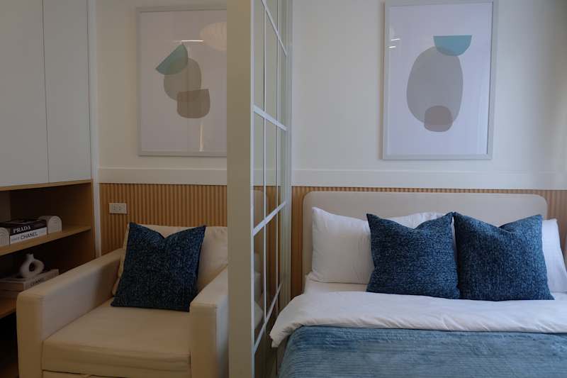 Cozy bedroom with a bed with a blue and white bed linen, two decorative pillows and a white armchair with a blue pillow.