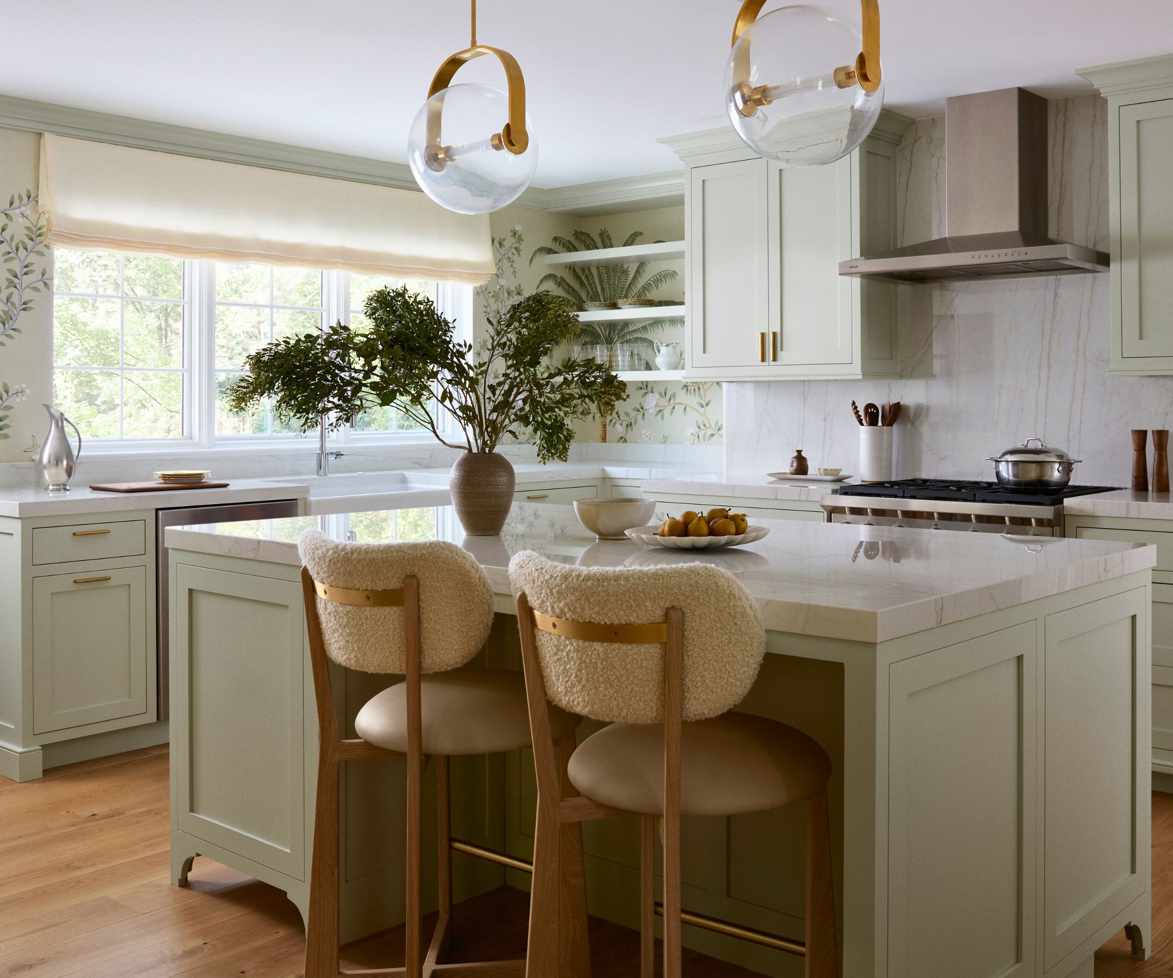 Kitchen with leaves wallpaper and light green cupboards and an island with a white marble worktop