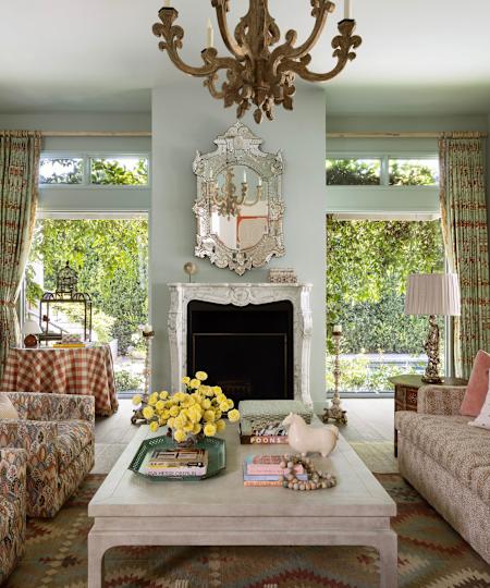 Living room with large windows, marble fireplace, decorated chandelier, Murano glass mirror and coffee table with yellow flowers and ornaments