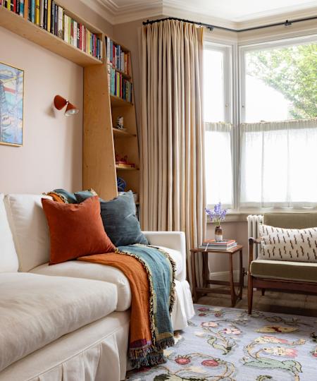 Living room with an bay window, peach walls, cream -flicking sofa with orange throwing, wooden book trade and mid -Century -chair