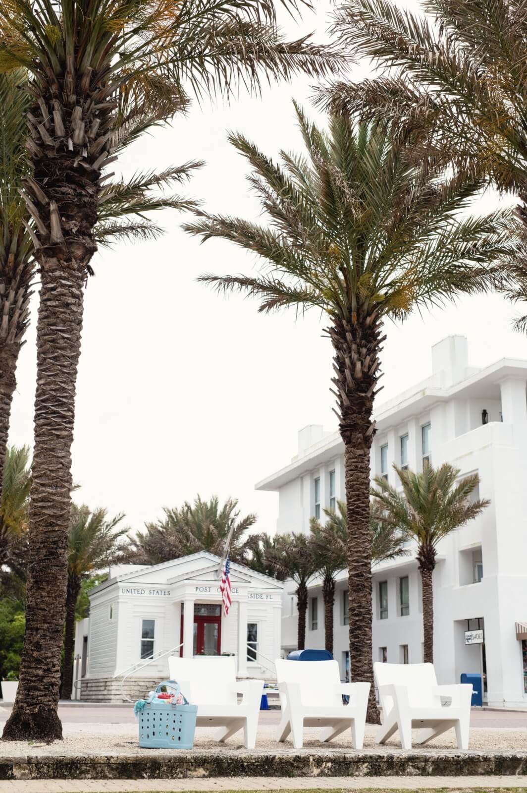 From Yeti to Seaside, this TX -based entrepreneur makes waves - 3 A white post building with a US flag stands behind palm trees and white outer chairs from Tupelo. In the foreground is a laundry basket and captures the relaxed charm of Sara Kenton's design.