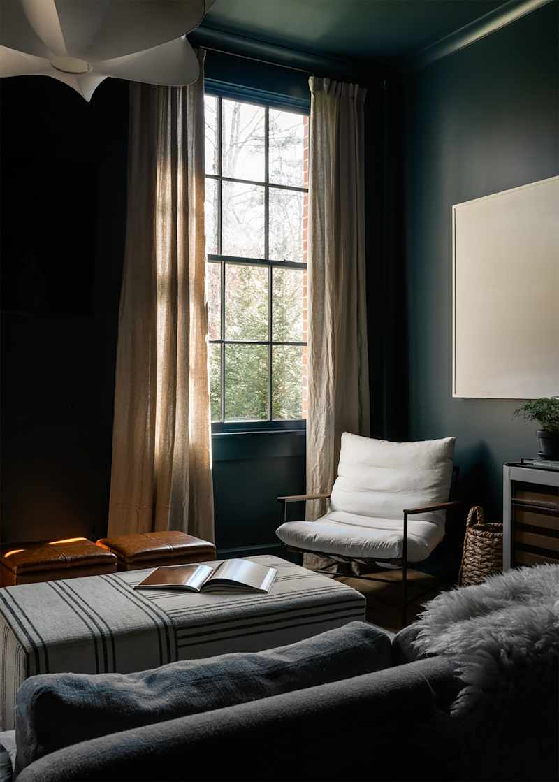 A modern apartment/loft, dark blue painted. The living room includes a comfortable white chair, an Ottoman, wine fridge and a large sofa.