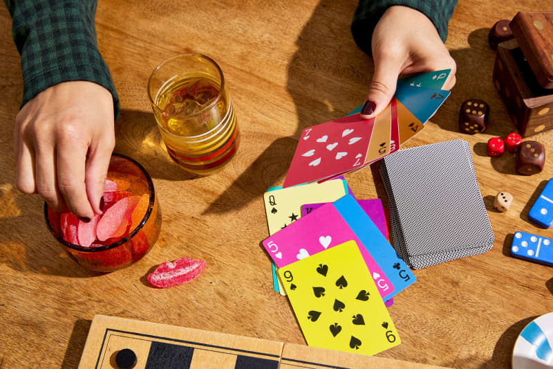 Hands of someone who plays cards at the table. The cards are light and colorful. Snacks and other games on the table