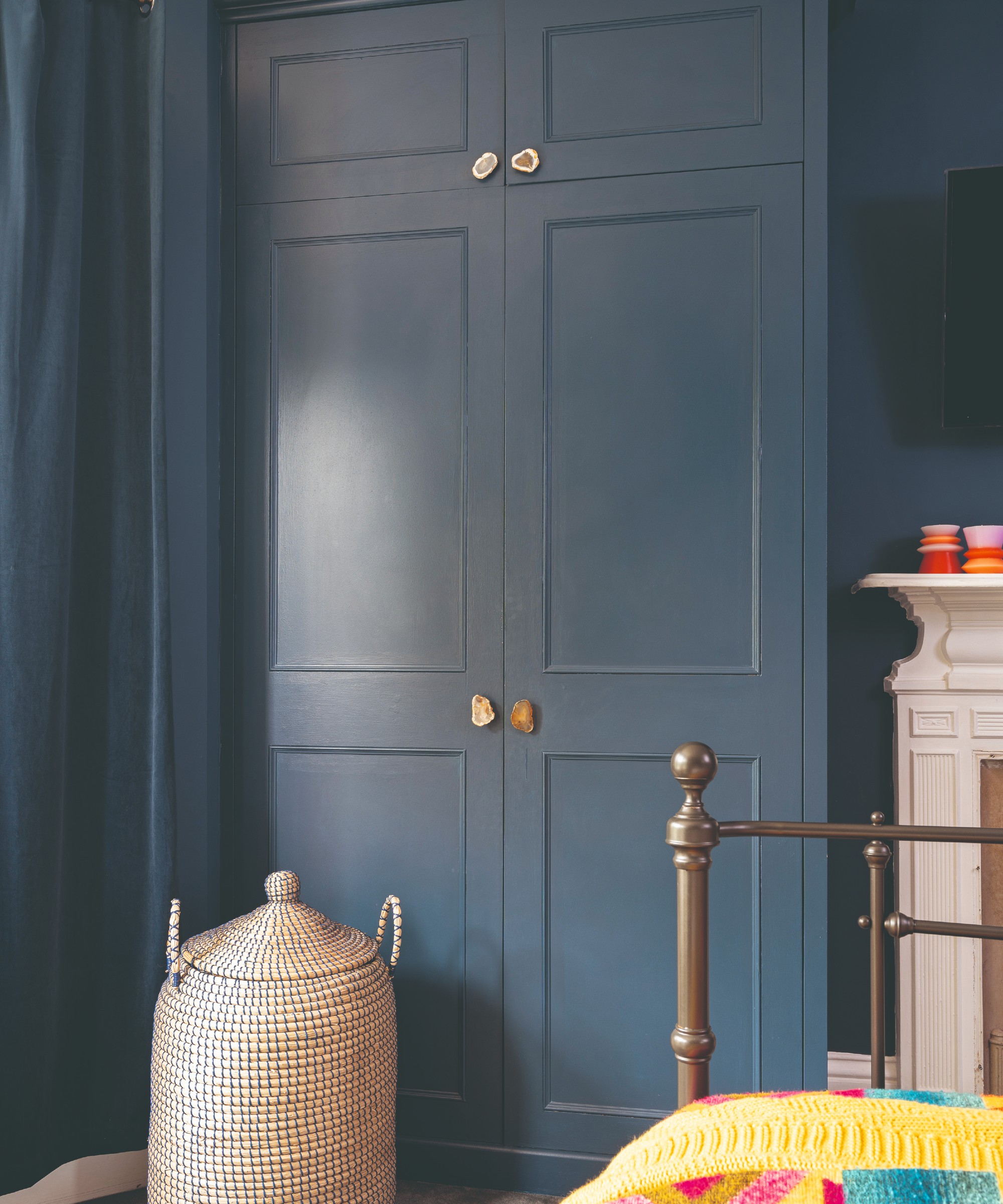 A bedroom with a dark blue wardrobe that corresponds to the walls and the curtains with quartz stone handles