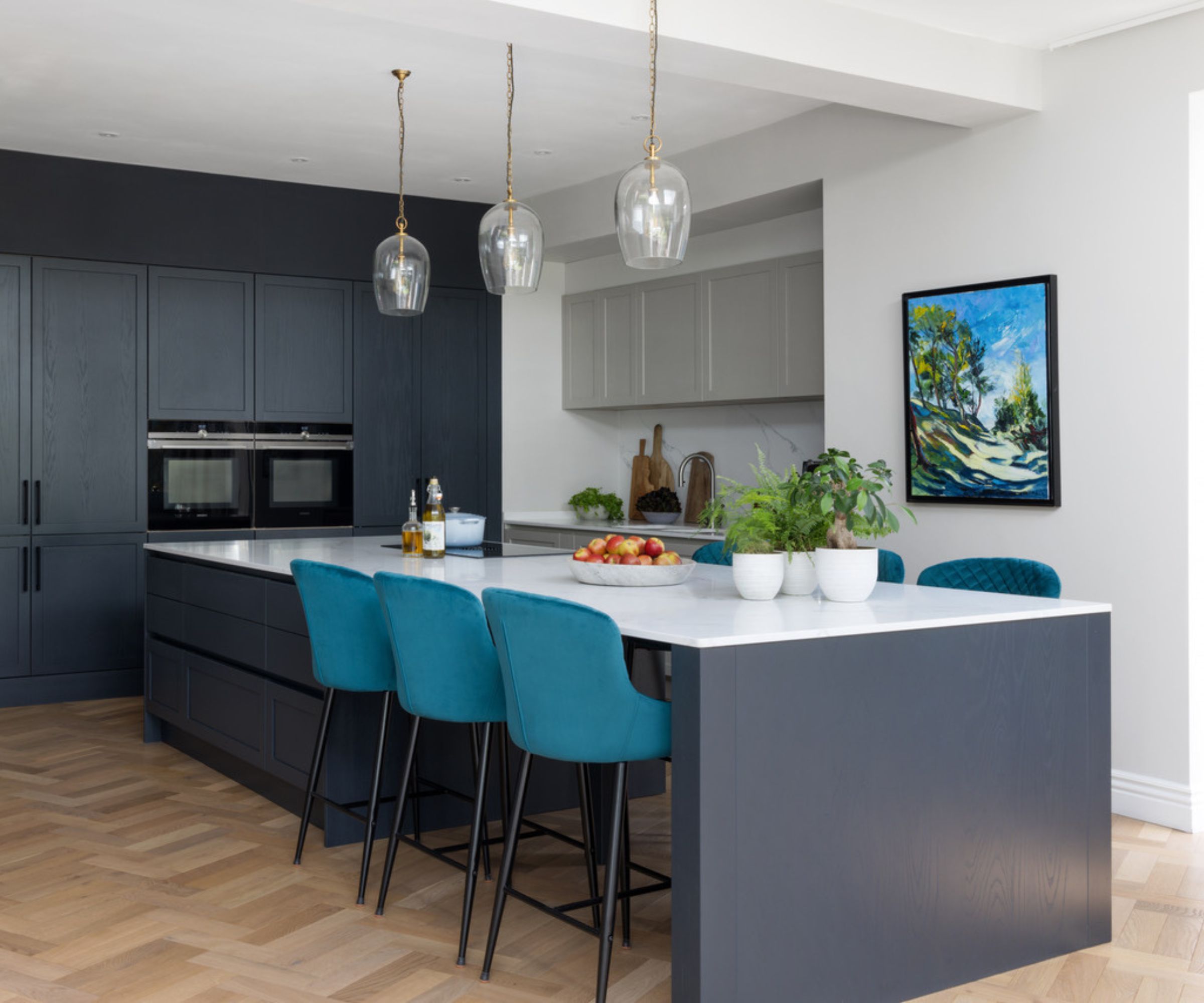 A large kitchen with dark blue cupboards and island, white marble slabs and wooden parquet base