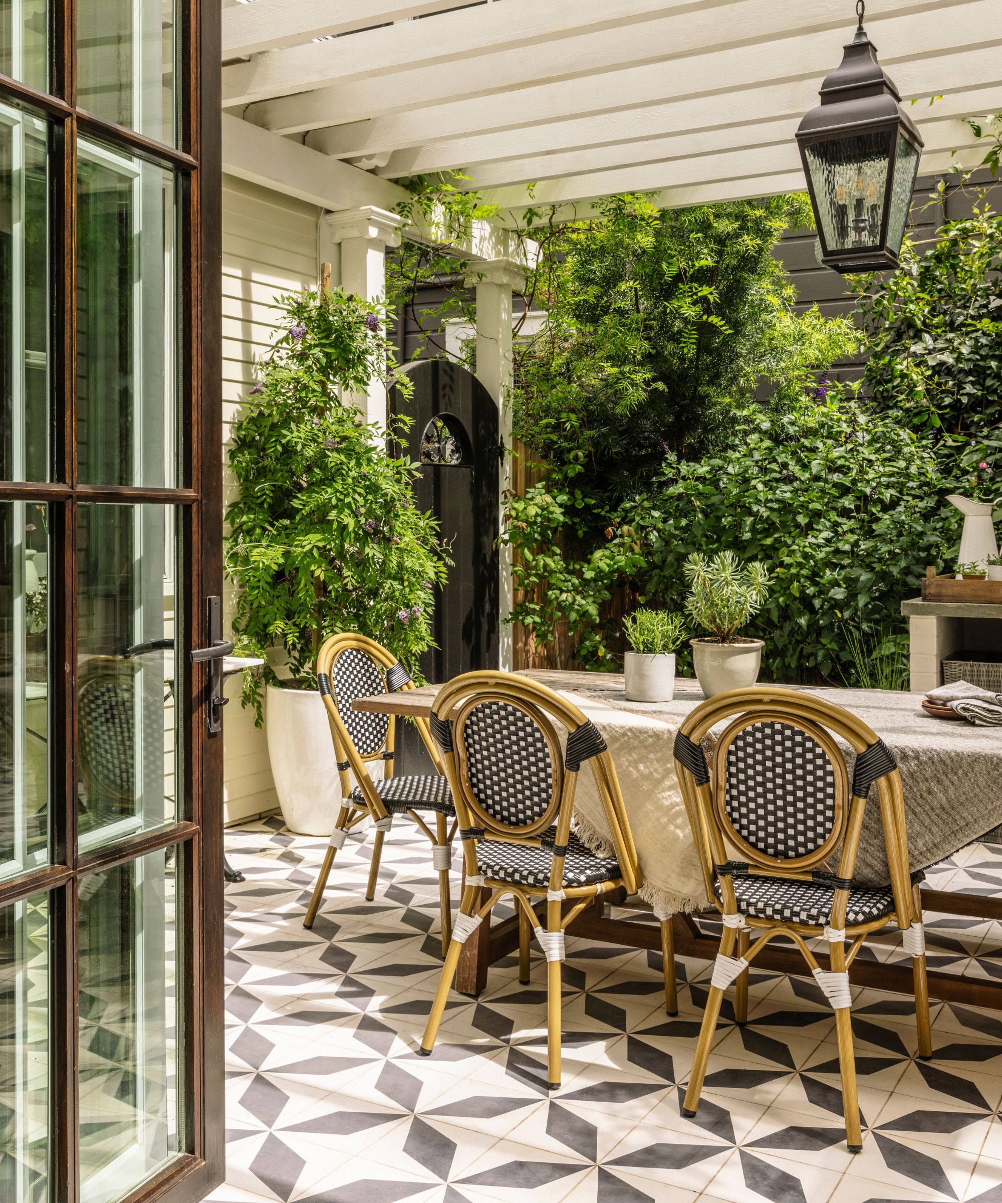 An outdoor dining area with patterned floor tiles and a large white pergola overhead