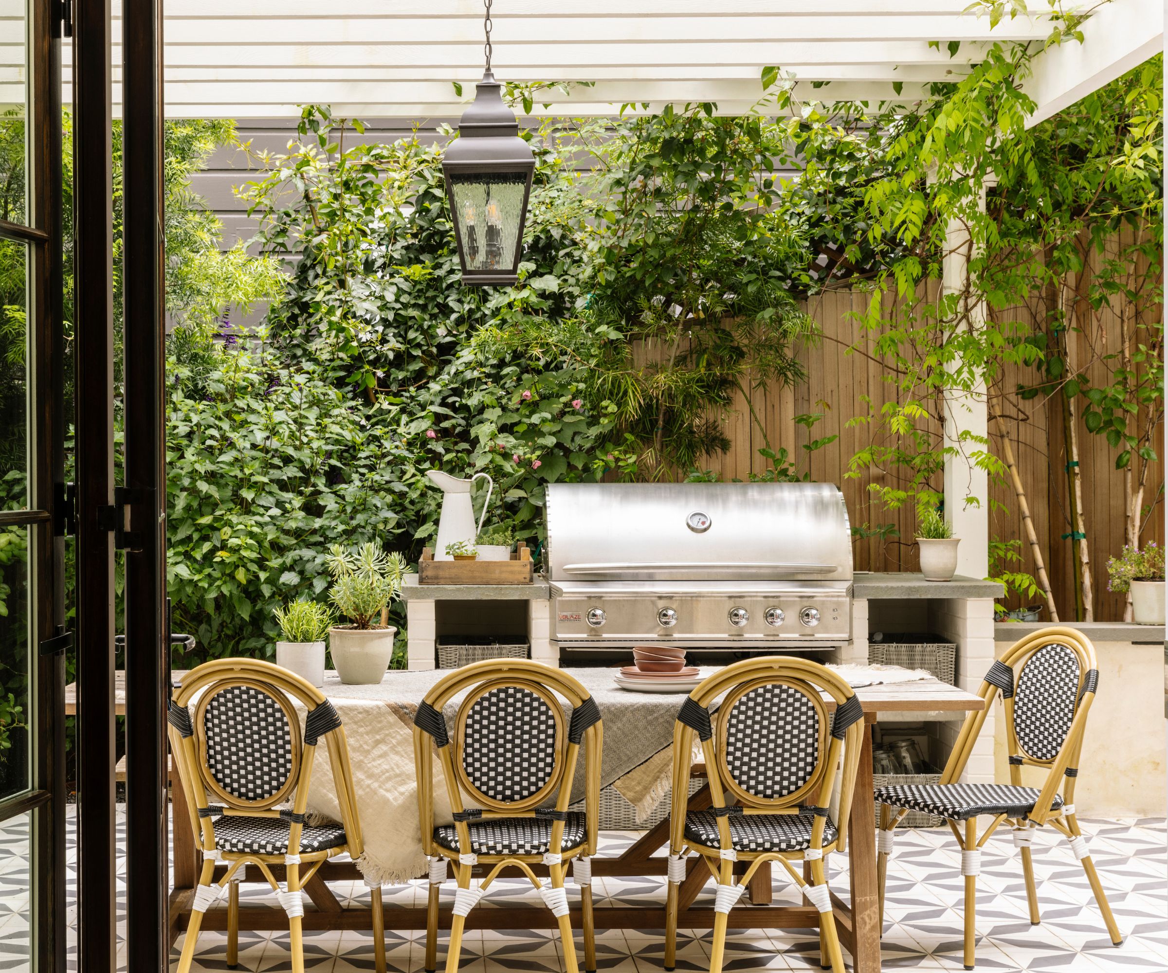 A kitchen and dining area outdoors with a stainless steel stone, patterned floor tiles and a wooden dining table