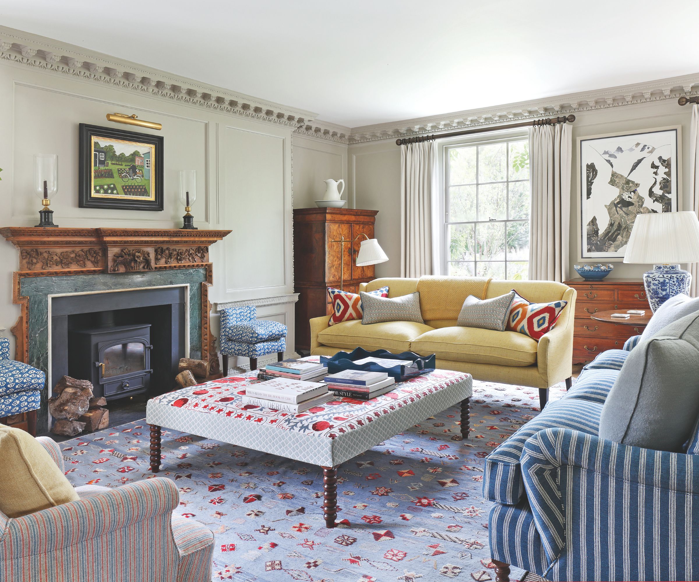 Traditional living room with large windows, a yellow couch and striped sofas that are around a padded coffee table