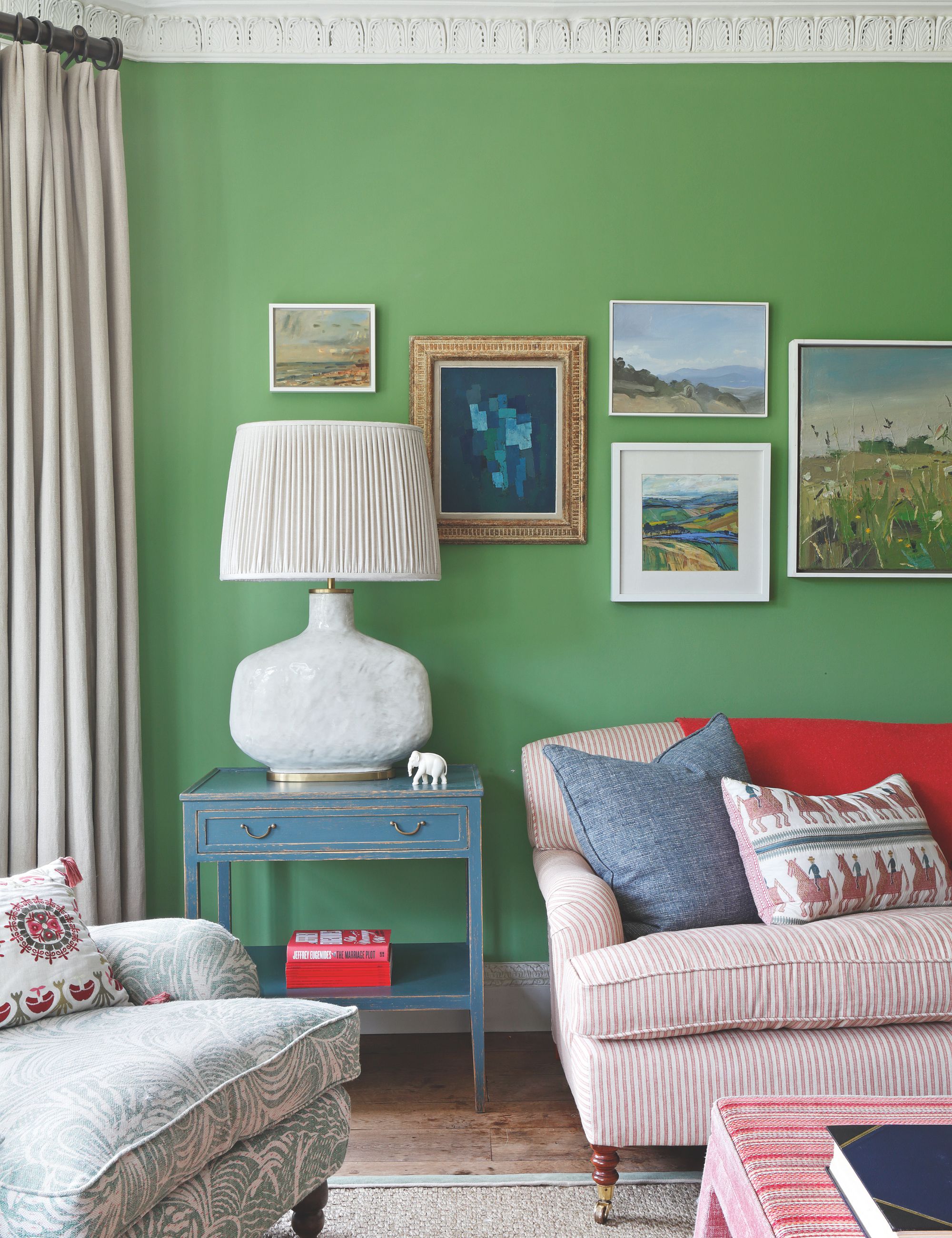 Green living room with gallery with a wall striped red and white sofa and a blue side table with a large lamp