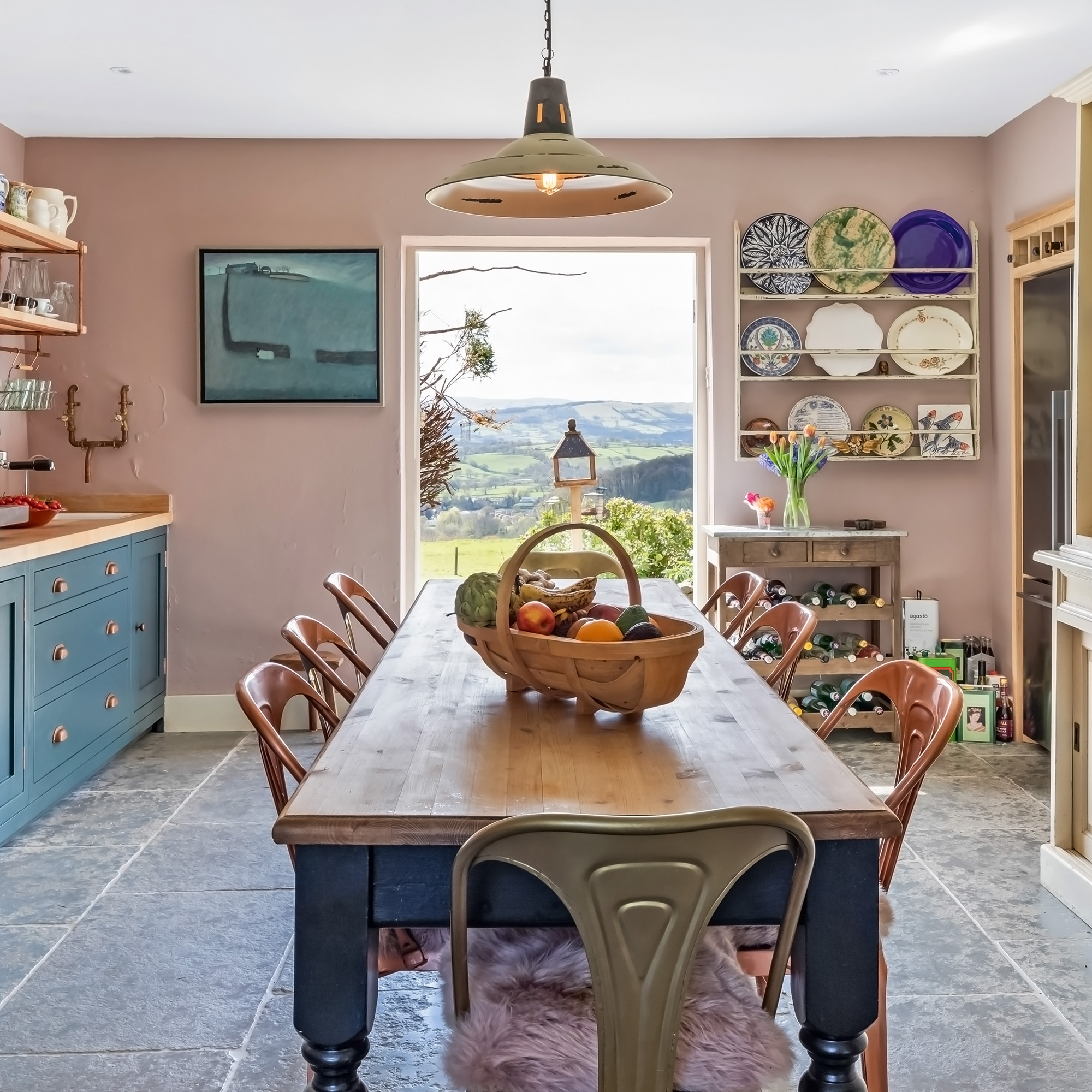 Country kitchen with a farmhouse table and metal chairs in the middle of the room with blue -painted cupboards