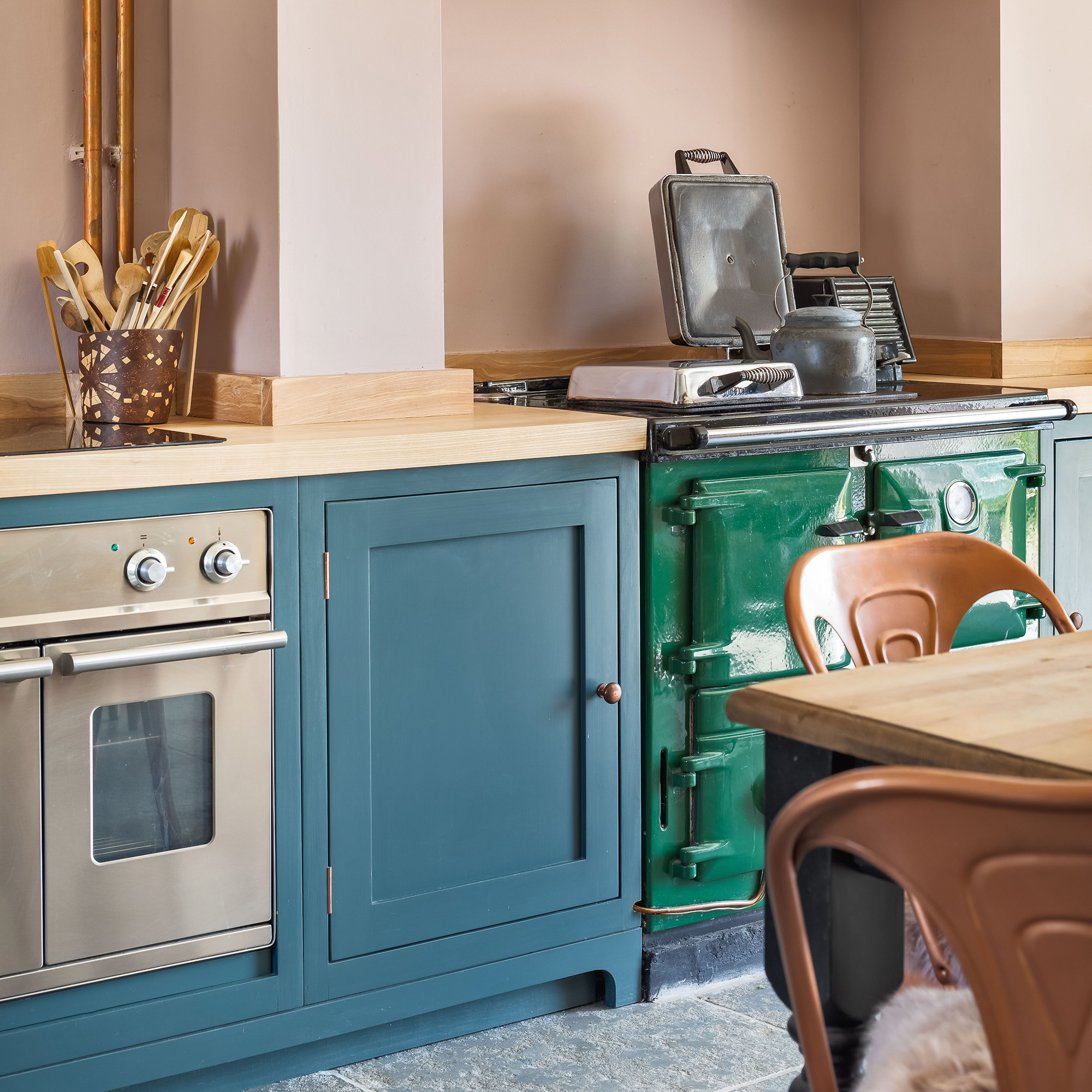 Blue -painted cupboards in the land kitchen with pink walls and stainless steel stove and green range stone kitchen