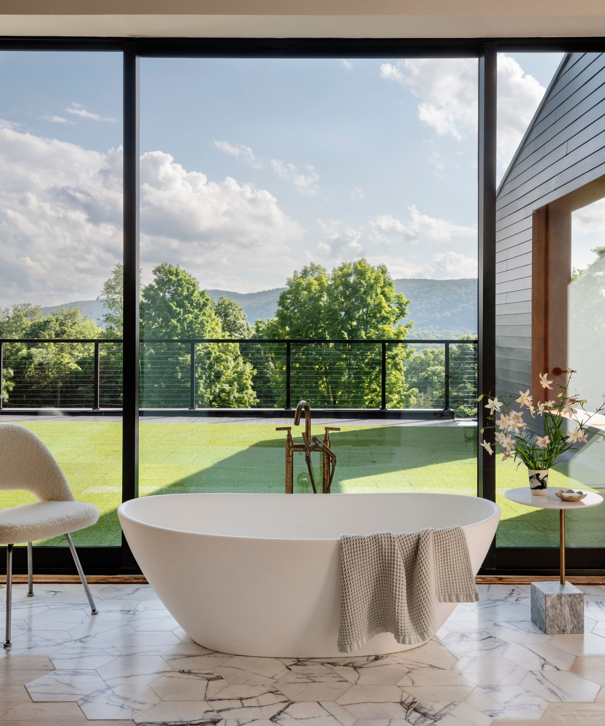 A free -standing tub in a bedroom with a boucle chair and a side table crowned with fresh flowers