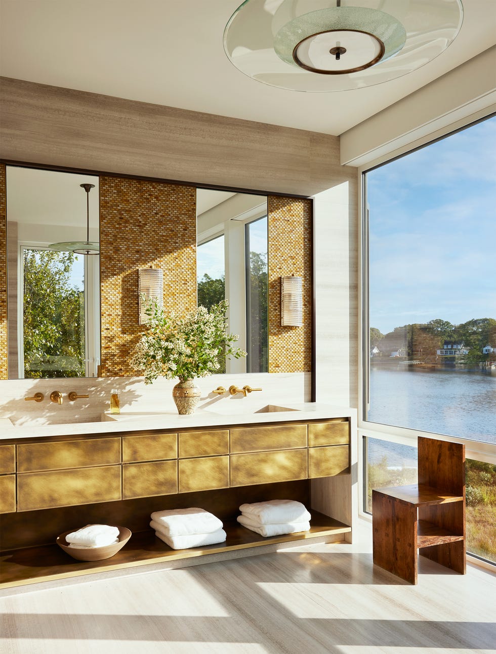 Modern bathroom with a view of water with a luxurious washbasin, decorative flowers and natural light.