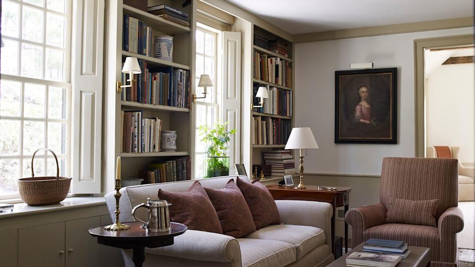 Traditional living room with lights, large windows and sofa with bookshelves and ancient paintings.