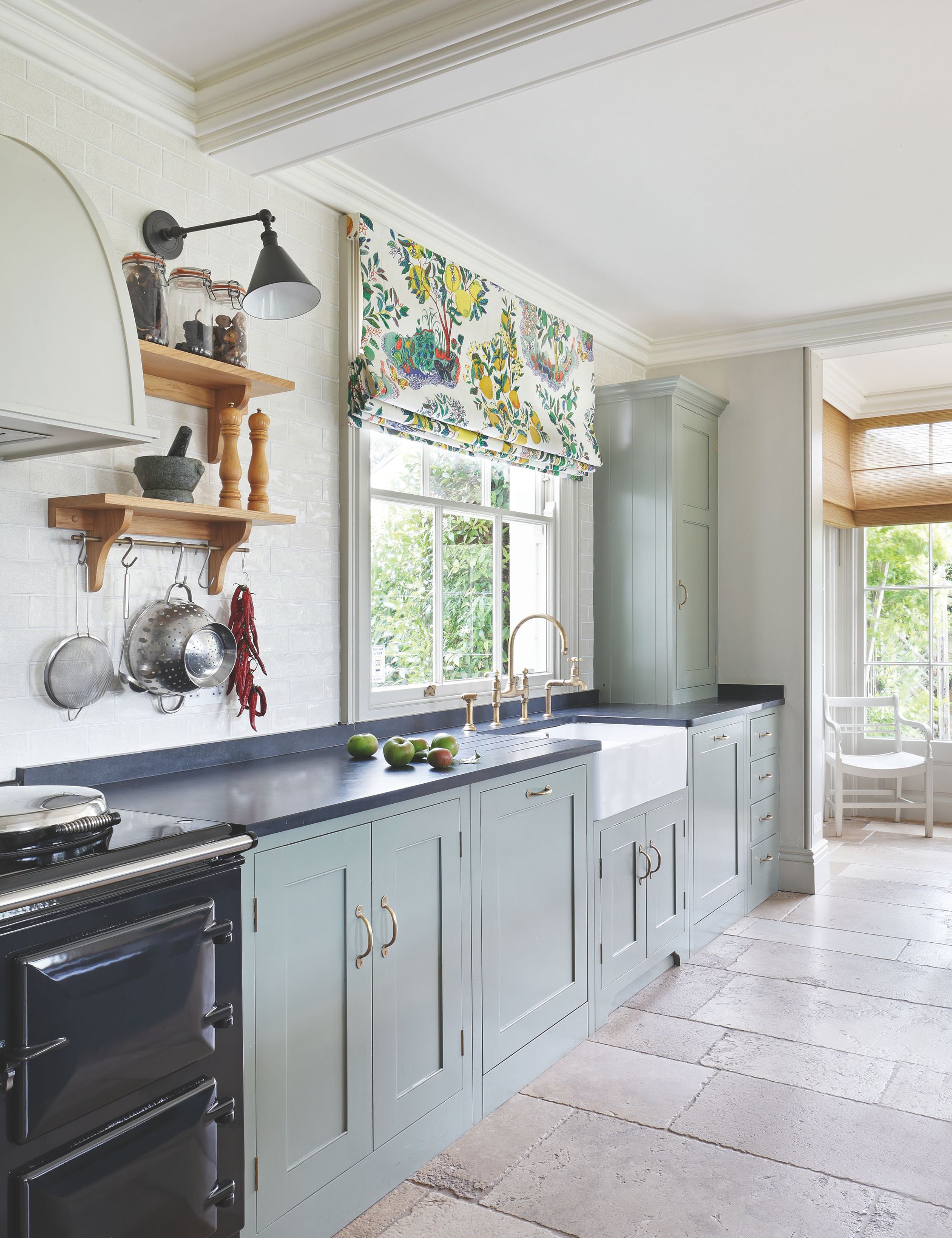 Light blue cuisine with stone floors and dark worktops with a window above the sink with a patterned blind