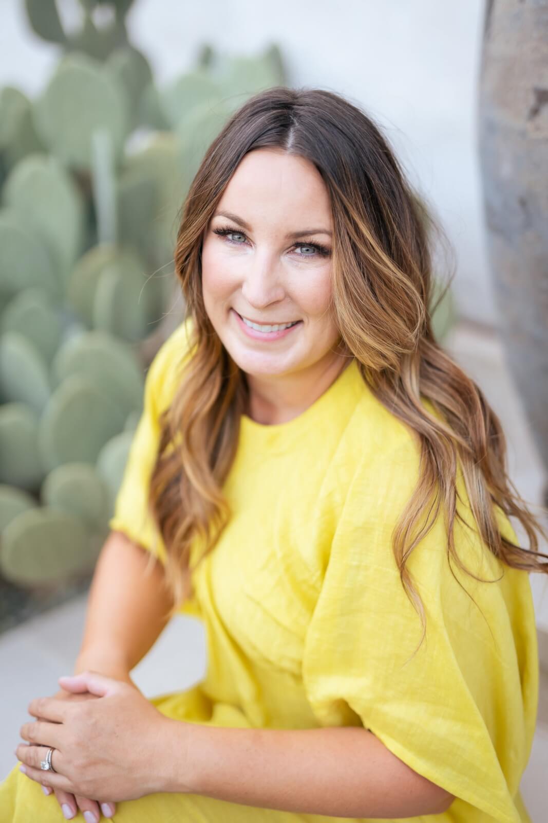 From Yeti to Seaside, this TX -based entrepreneur makes waves - 1 Sara Kenton with long brown hair sits outdoors in a bright yellow dress and smiles at the camera from green cacti.