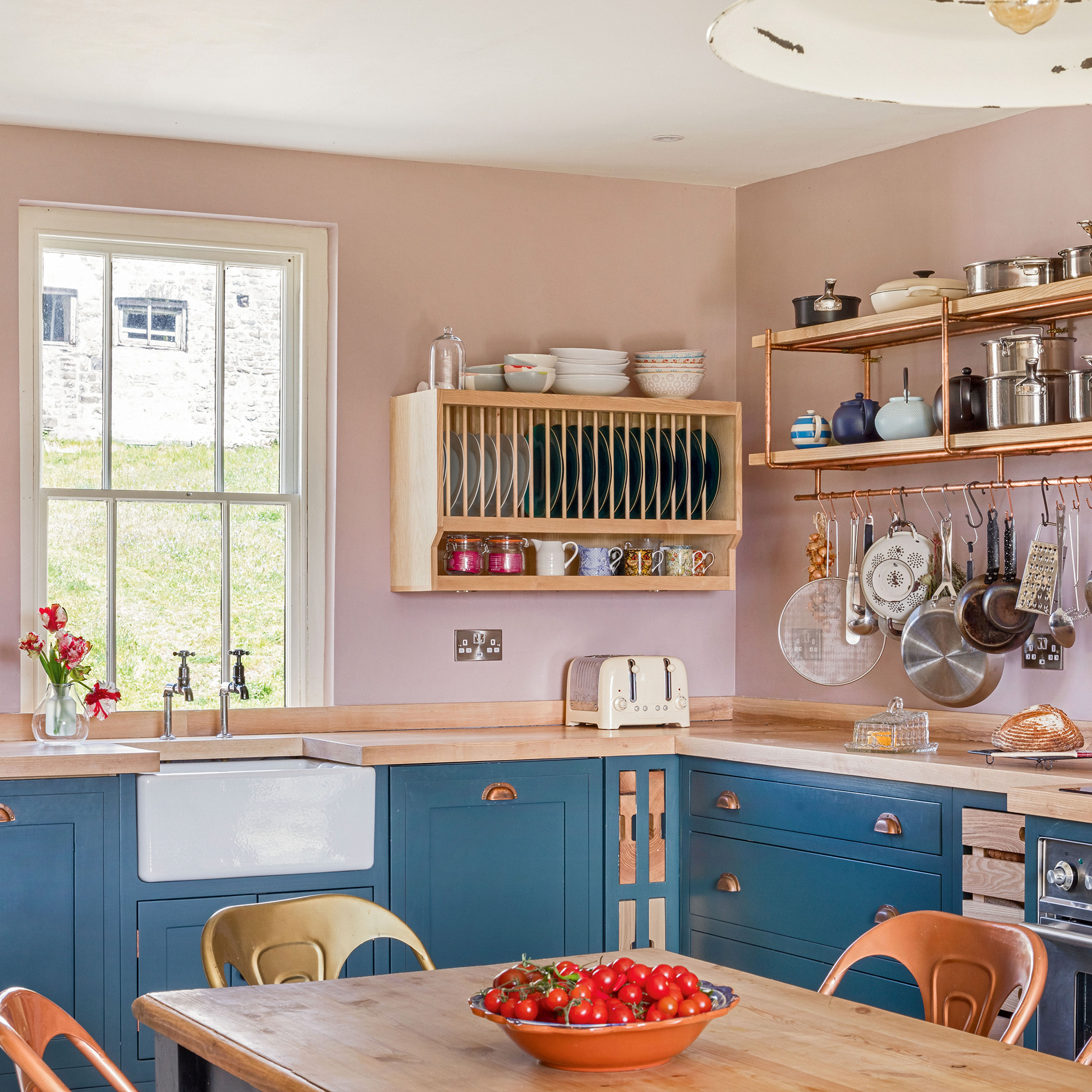 Country kitchen with pink wall and blue cupboards and white Butler's sink and ash panel shelf and open shelves