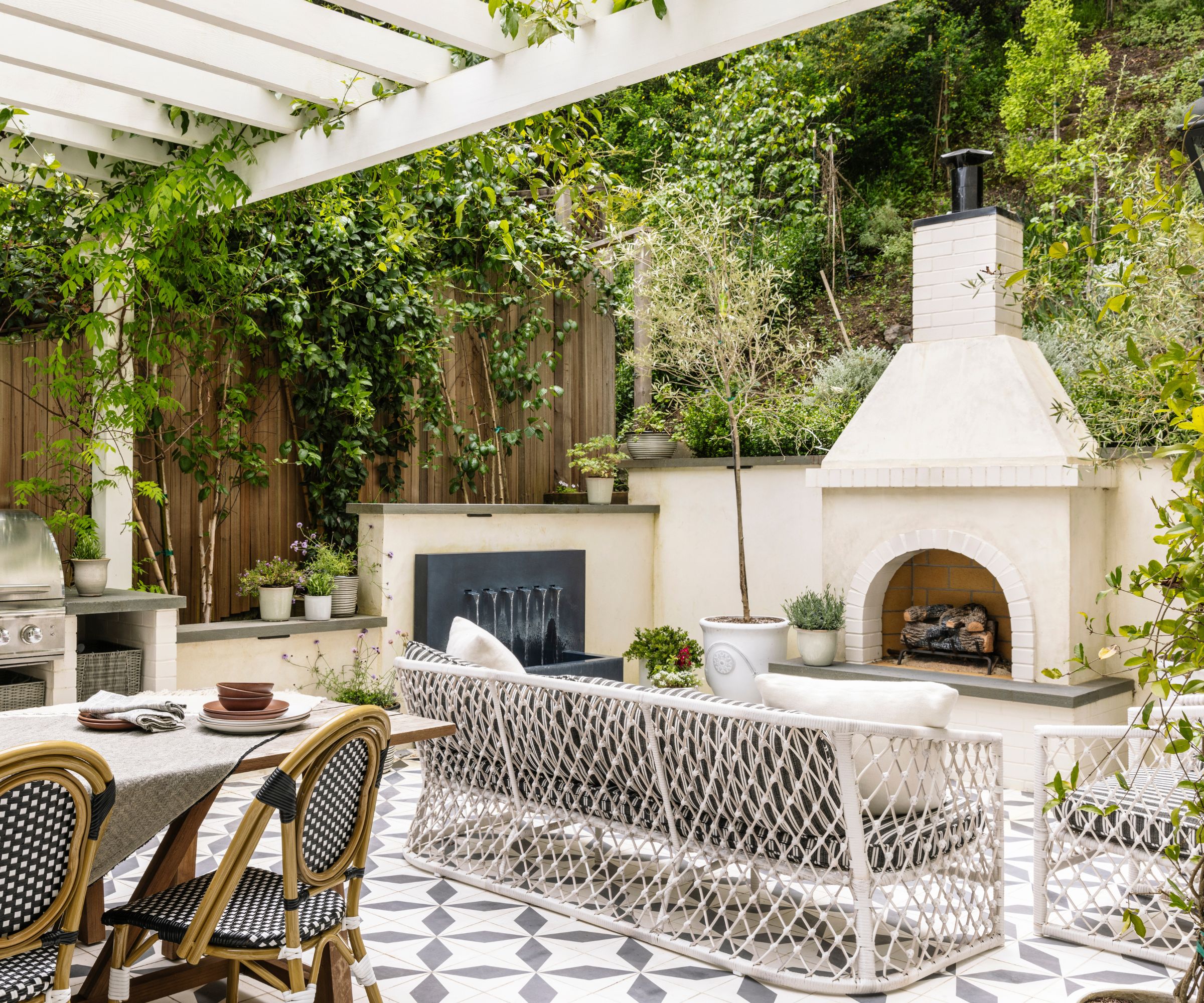 A outdoor living area with a large fireplace, patterned floor tiles, a water feature and furniture with a knotted design