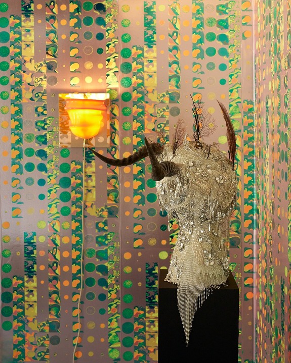 An abstract decorative sculpture on a base against a lively, patterned wall with a yellow ceiling light.