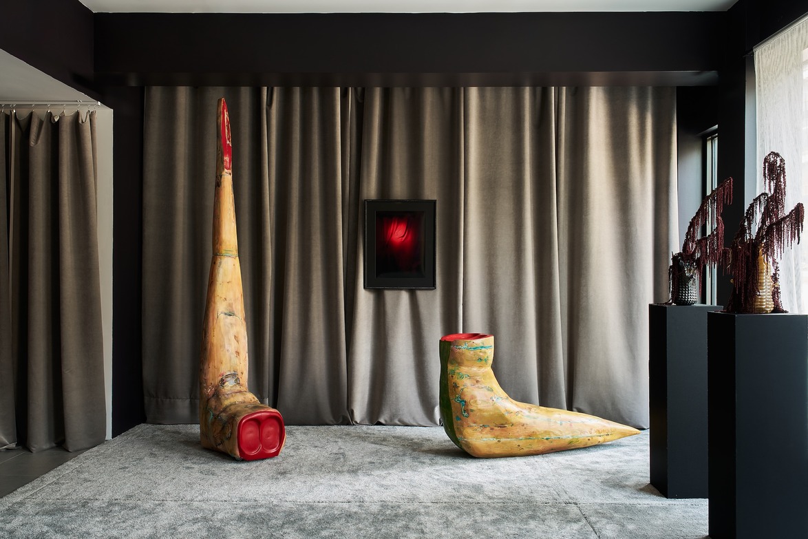 Contemporary art exhibition with abstract sculptures with living colors and textures in front of a curtain background.