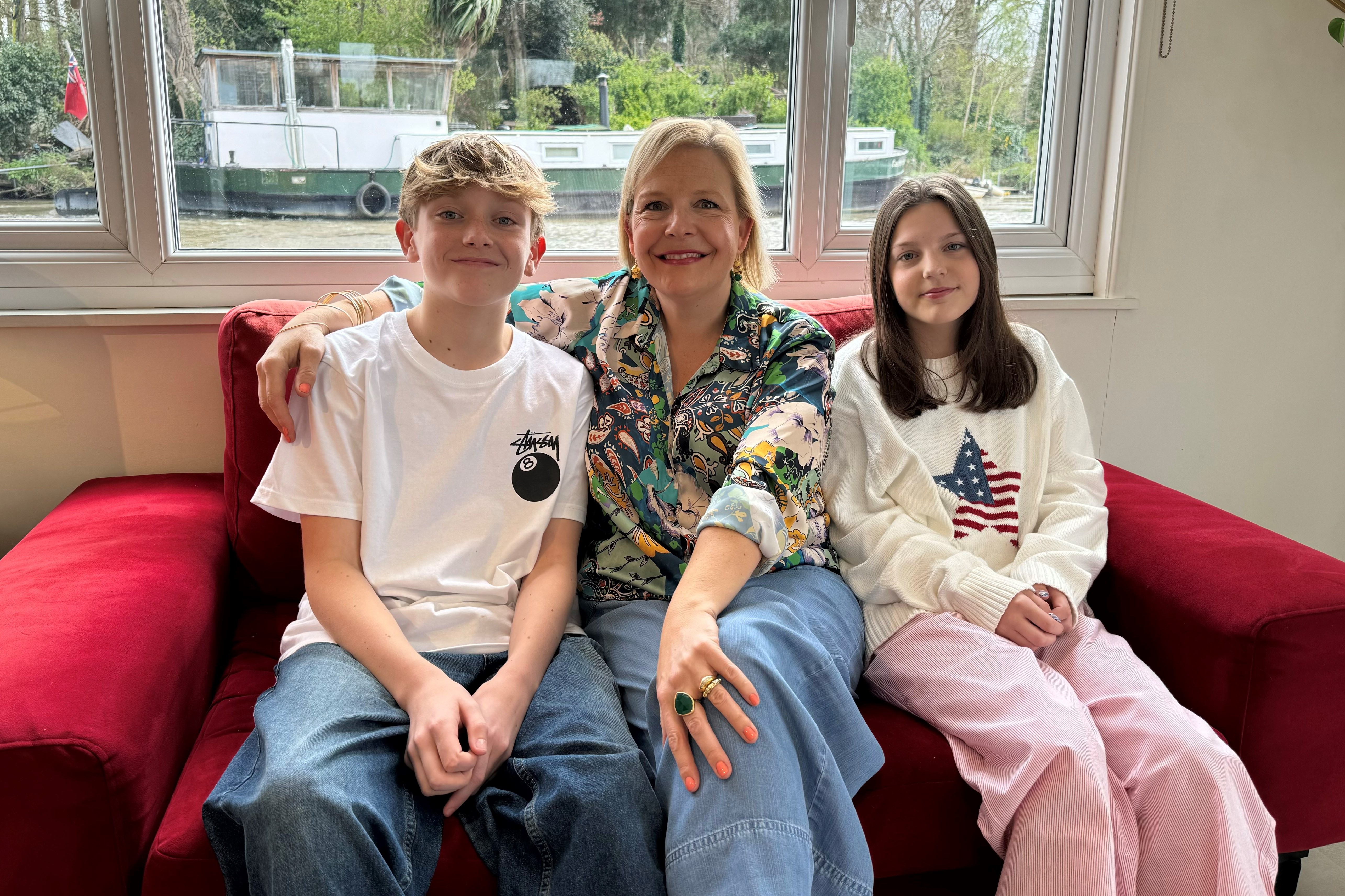 A woman and two children sit on a red couch.