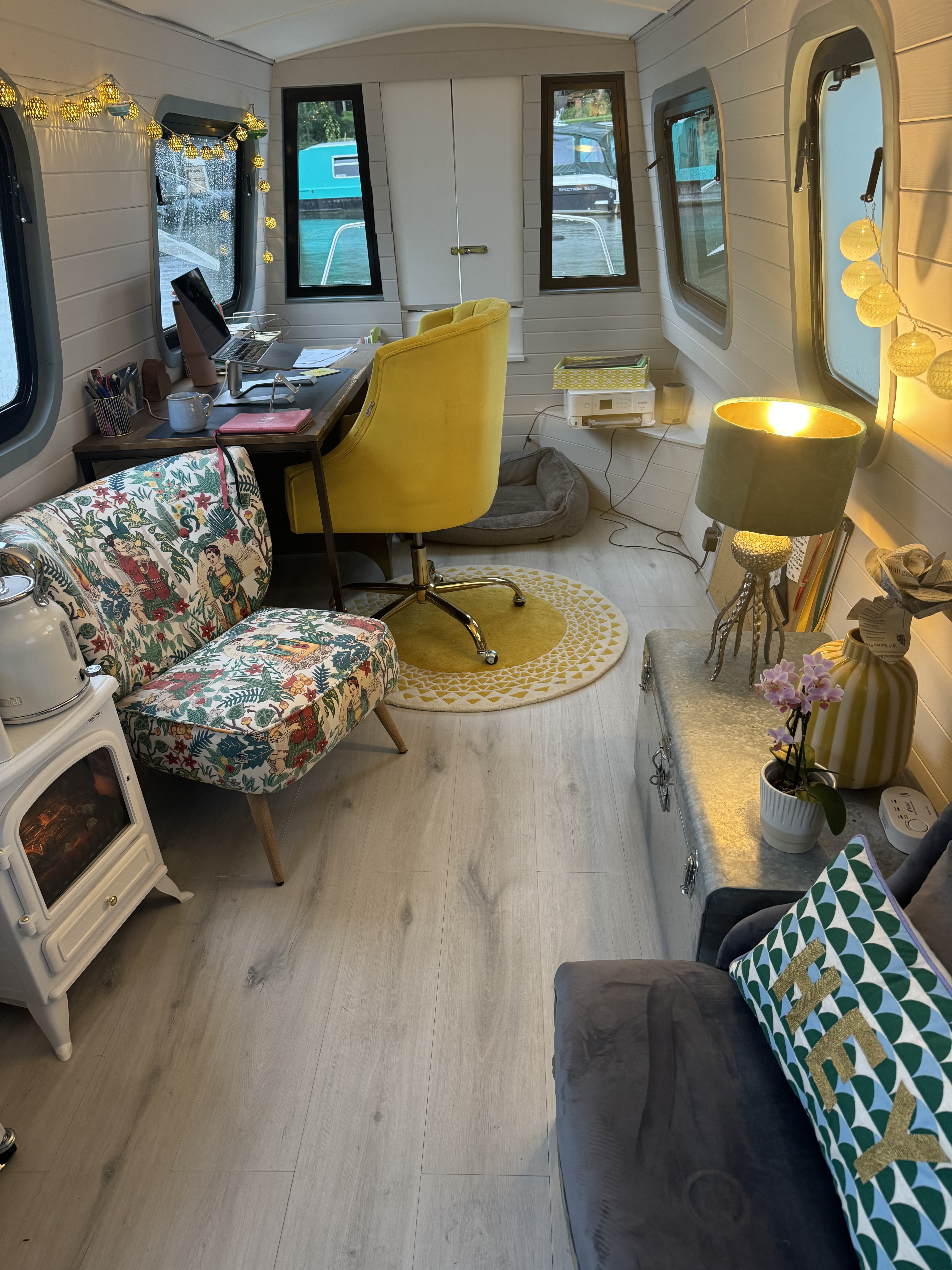 Interior of a narrow boat with a work area, a seating area and a small electric fire.