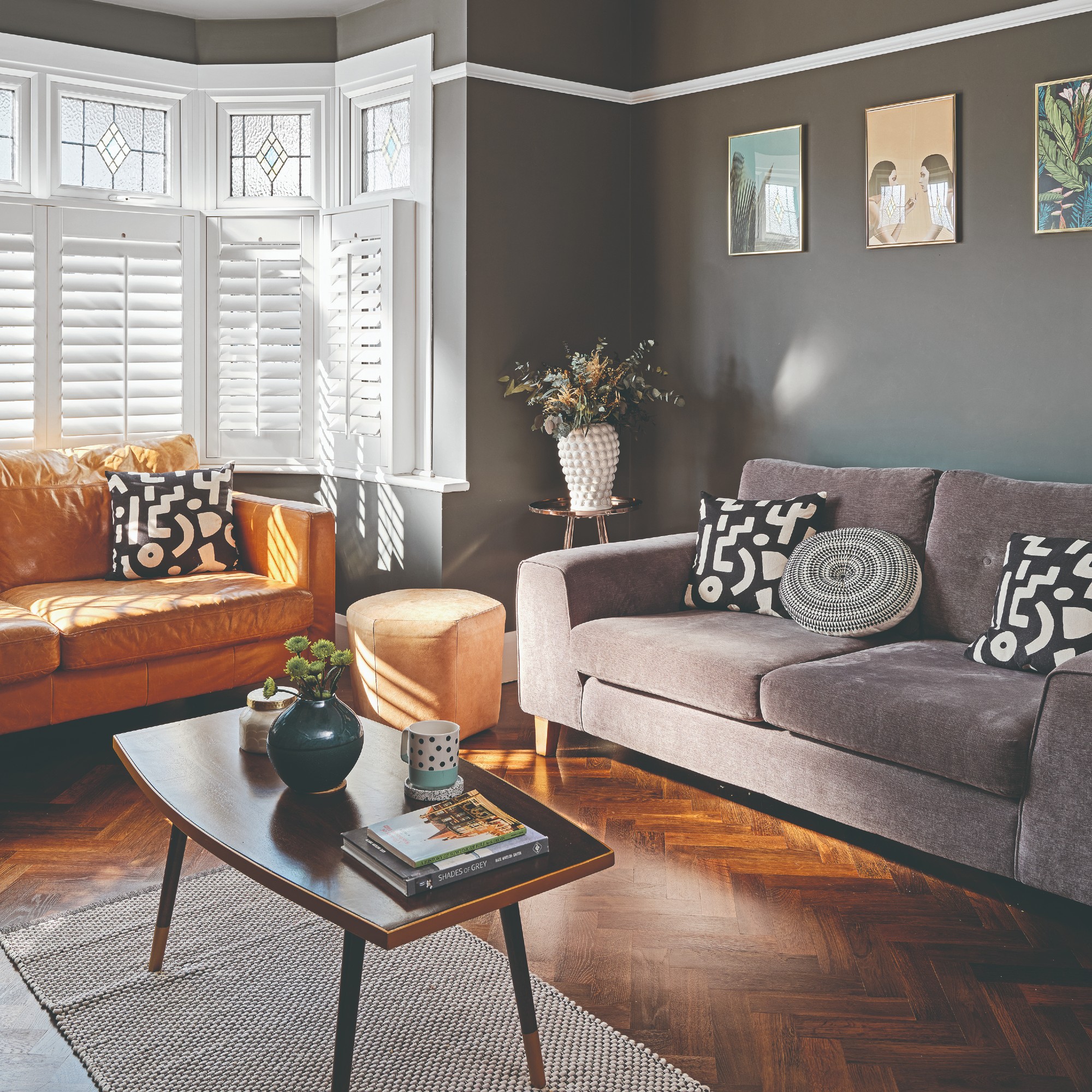 A dark, gray living room with a gray velvet sofa, a brown leather sofa and a small stool