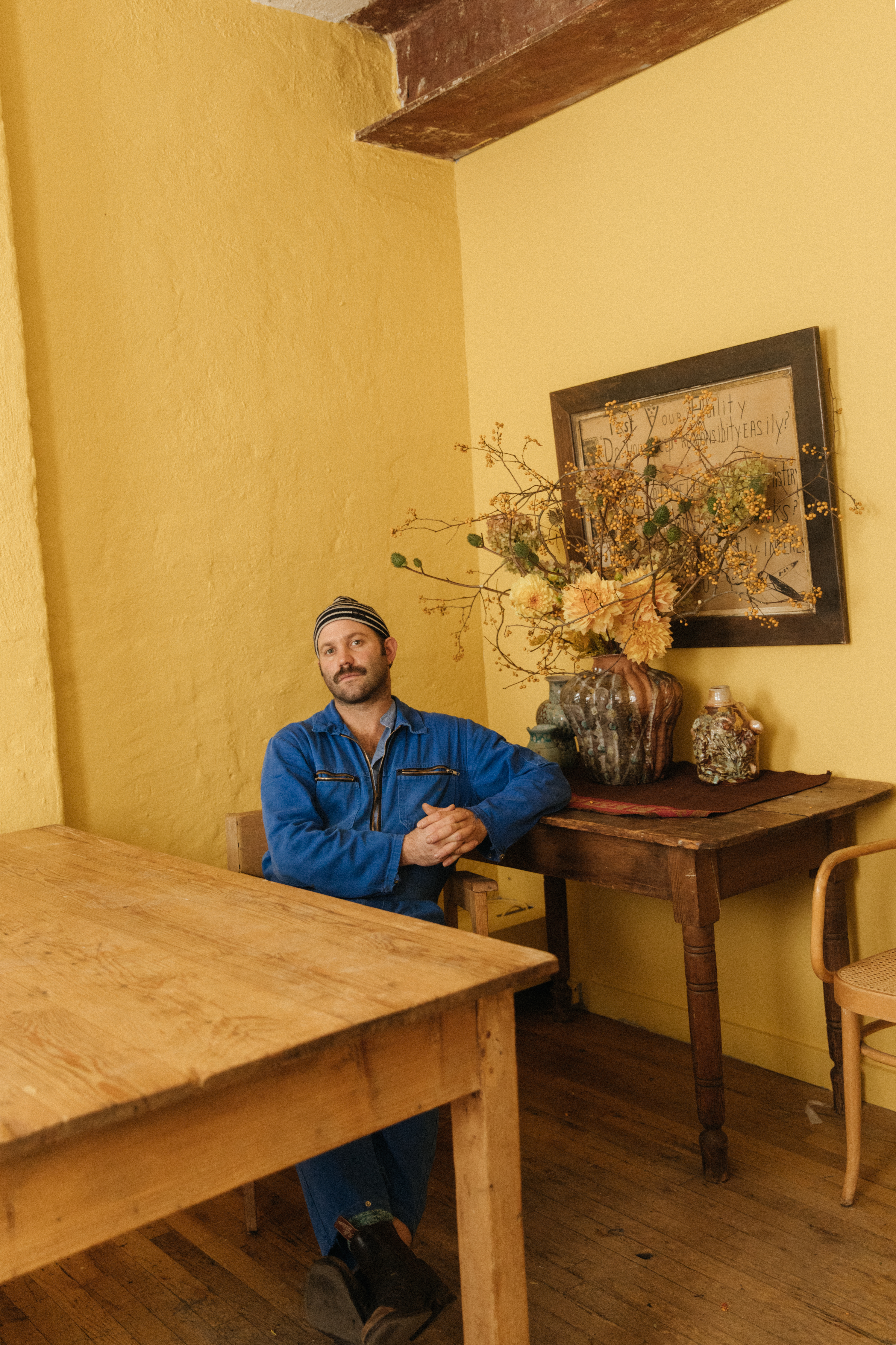 Curator Alex Tiighi Walker sits in a yellow room at a table