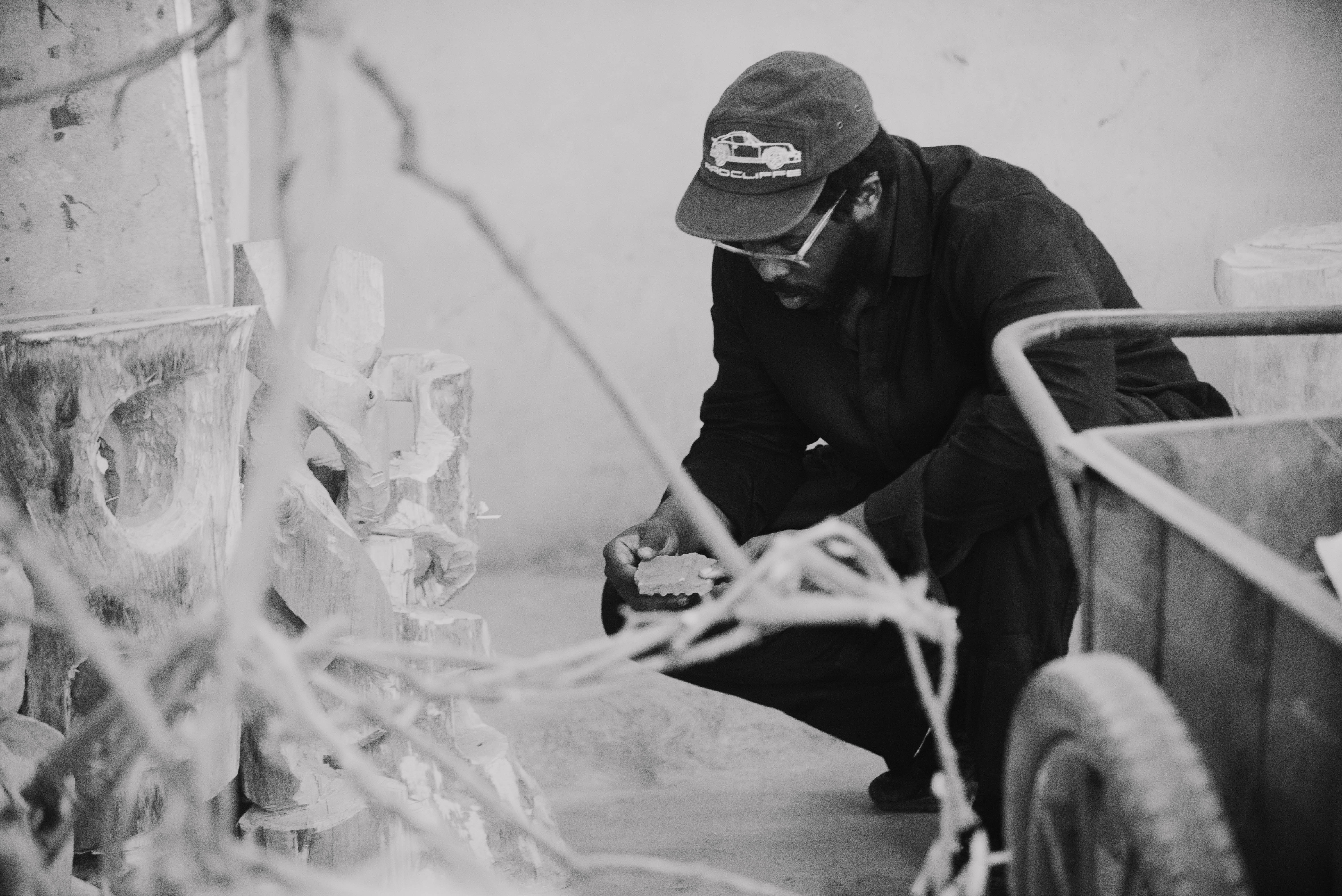 Designer Myles Igwebuike crouches on the ground next to works of art