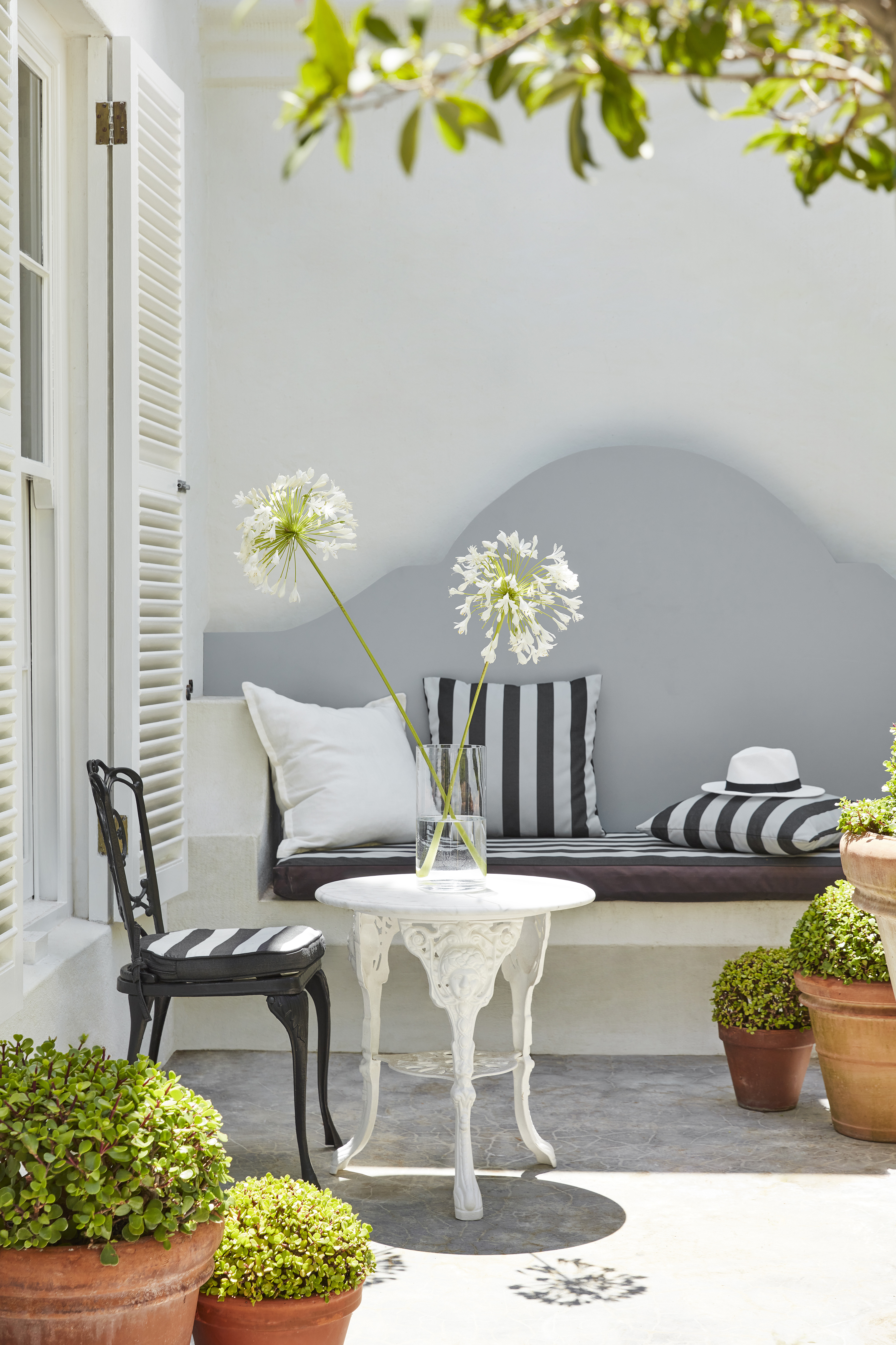 Little Greene outer color in a very light blue, painted seating area outdoors. There is a café and a bank seat against the wall.