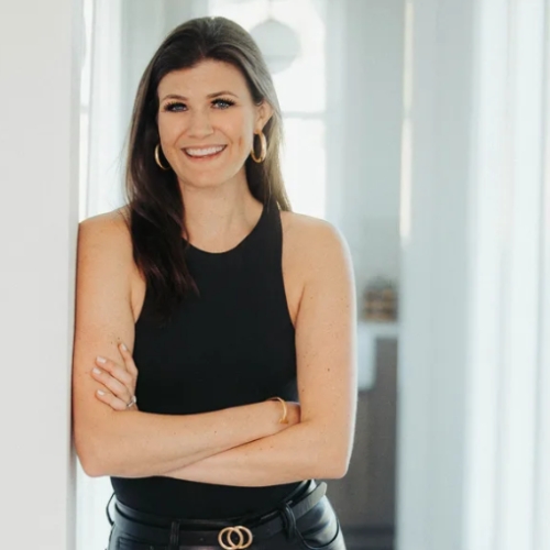 Image of a woman in a black top and pants that lean against a white wall.