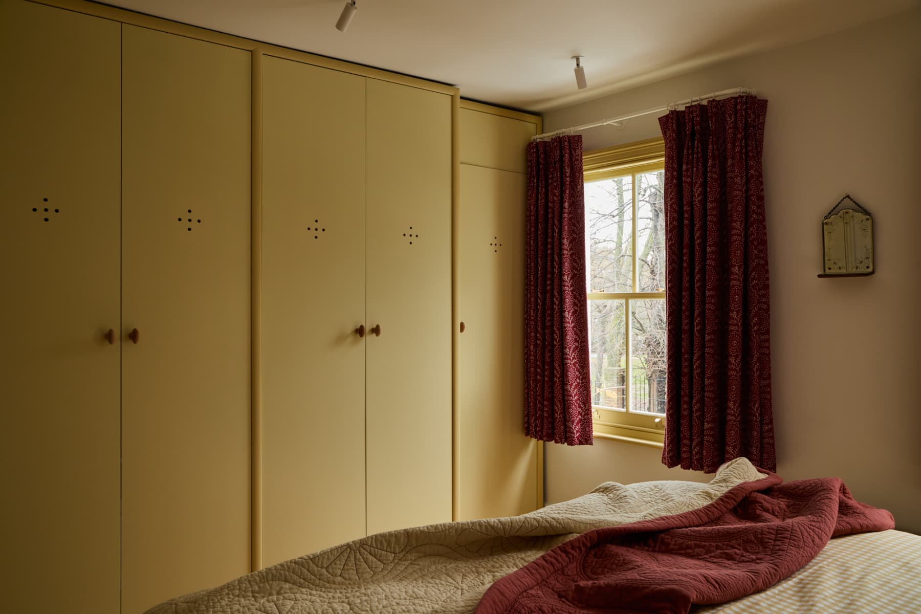 Yellow bedroom with short red curtains, beige walls and yellow amounts with a red ceiling