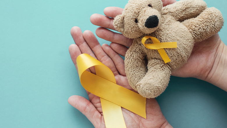 Persons who hold gold straps and teddy bear for the awareness of cancer in children