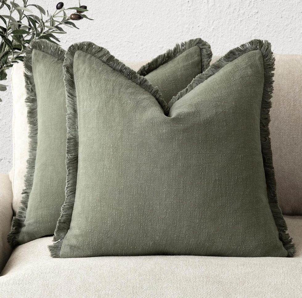 Two green pillows on a beige sofa with leaf decor in the background.