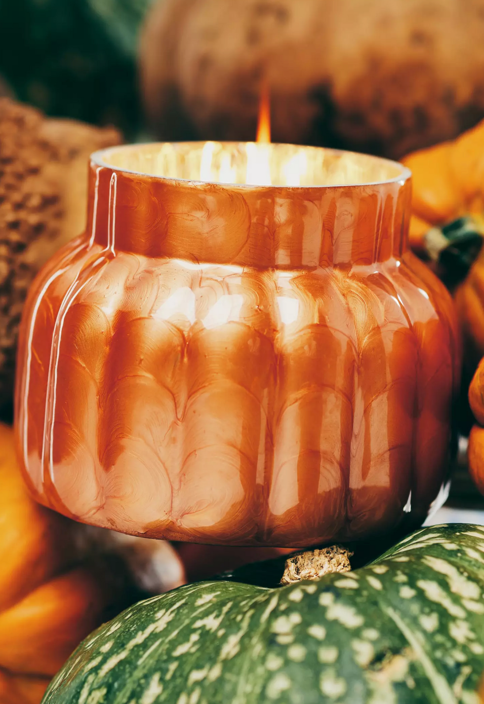 Orange candle in a pumpkin form surrounded by pumpkins.
