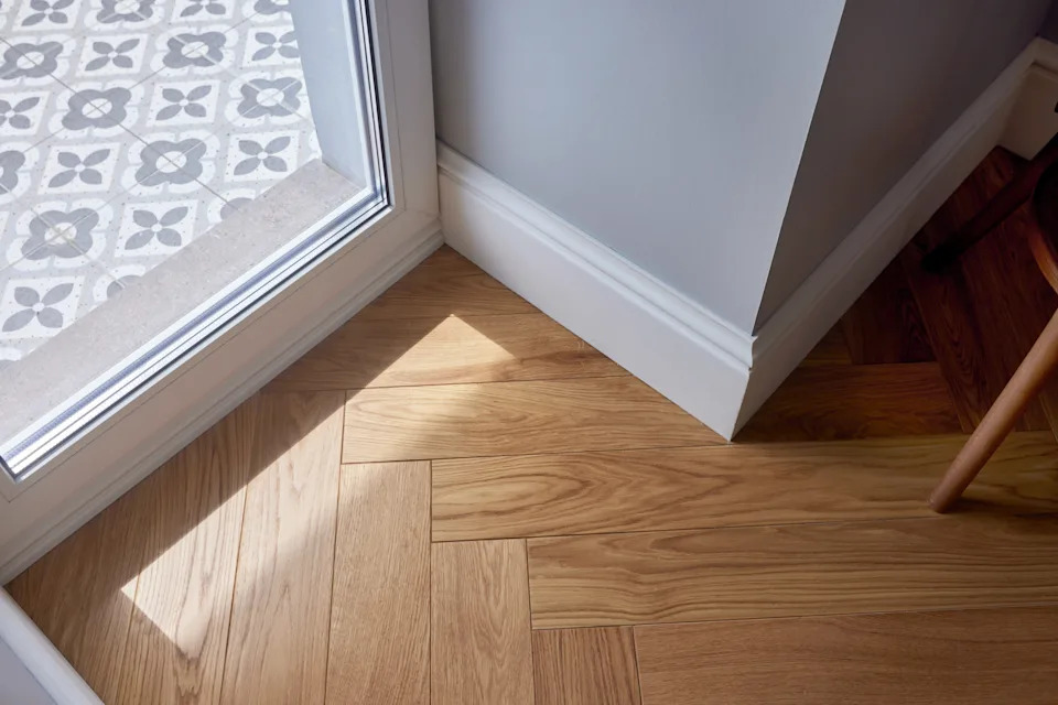 The sunlight filters through the glass door and illuminates a cozy corner with a wooden floor and a stylish, tiled entrance. This contemporary design radiates heat and invites an inviting atmosphere into the room